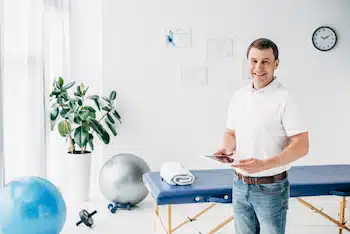 smiling-chiropractor-holding-digital-tablet-in-hospital-and-looking-at-camera